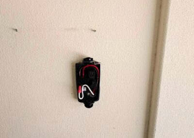 A wall-mounted electrical box with exposed wires is visible on a beige wall. The cover is missing, showing red, white, and black wires connected inside the box.