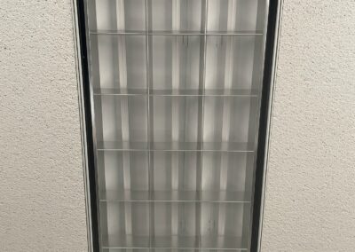 A rectangular fluorescent ceiling light fixture, viewed from below, is set into a speckled drop ceiling. The light appears to be off, but some green components are faintly visible inside the fixture.