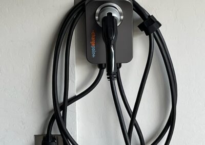 A wall-mounted electric vehicle charger with a coiled black charging cable neatly wrapped around the unit, plugged into a nearby wall outlet.