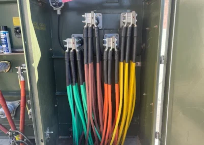 An electrical panel with several thick colored cables—green, brown, yellow, and orange—connected to terminal blocks inside the cabinet. The cables are neatly organized and run vertically.